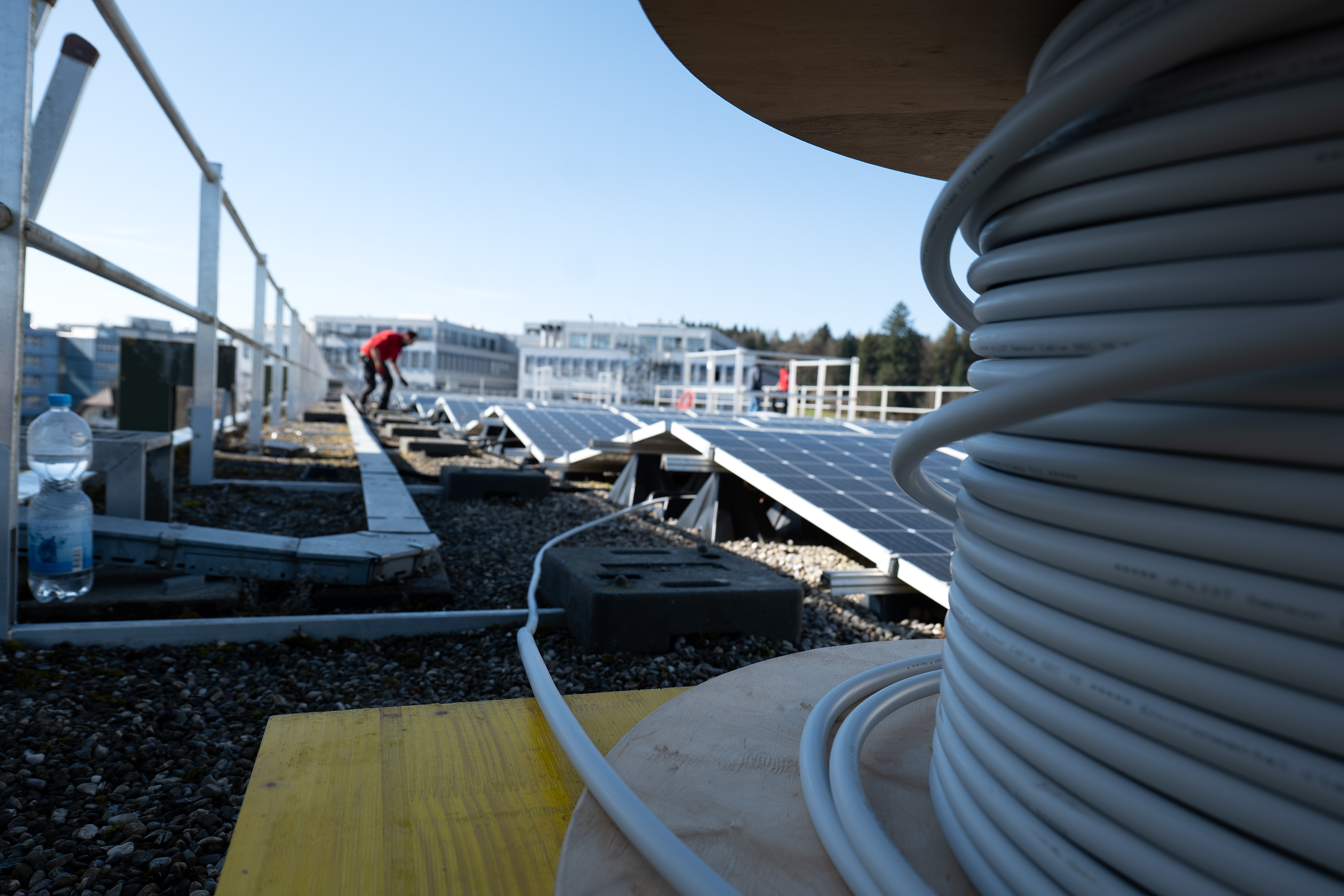 Sicht über ein Dach mit zwei Mittarbeitenden die an einer PV Anlage arbeiten.