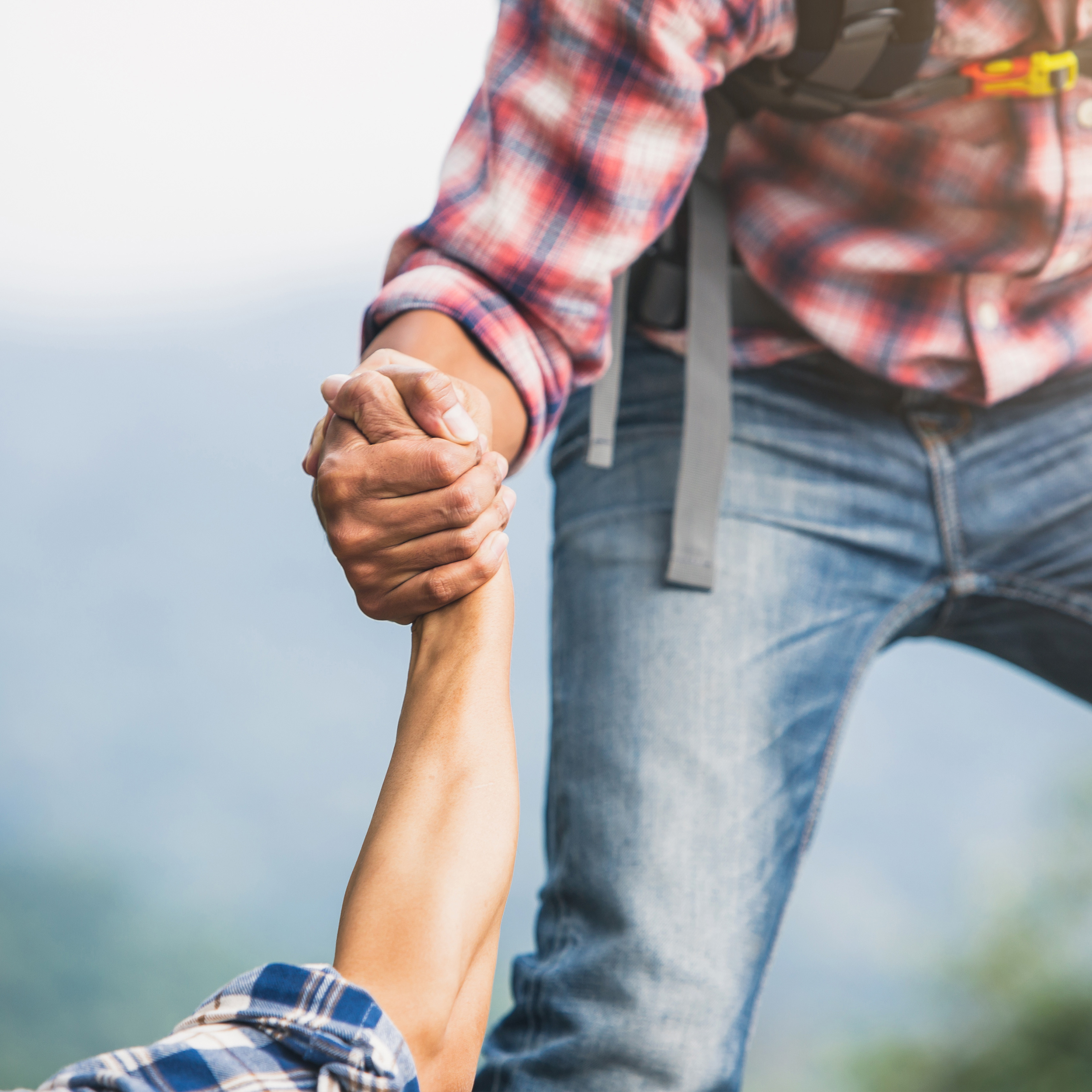 Eine Person die eine Andere an der Hand nach oben zieht